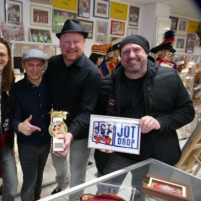 Die Bandmitglieder von Jot Drop stehen im Troisdorfer Karnevalsmuseum und präsentieren ihren ersten Närrischen Oscar, den sie dem Museum stiften.