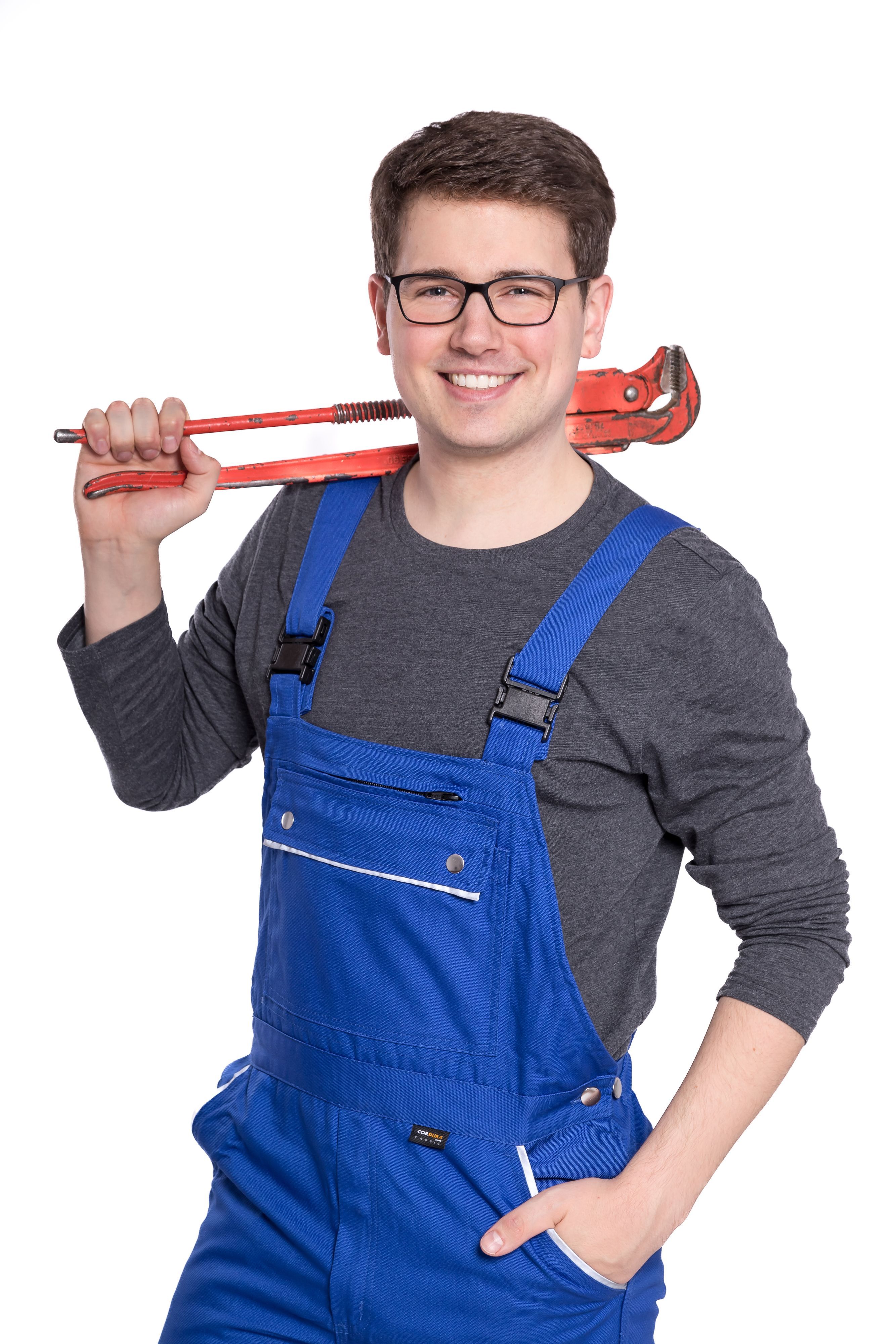 Ein Mann im Blaumann hat eine Zange geschultert und grinst in die Kamera.