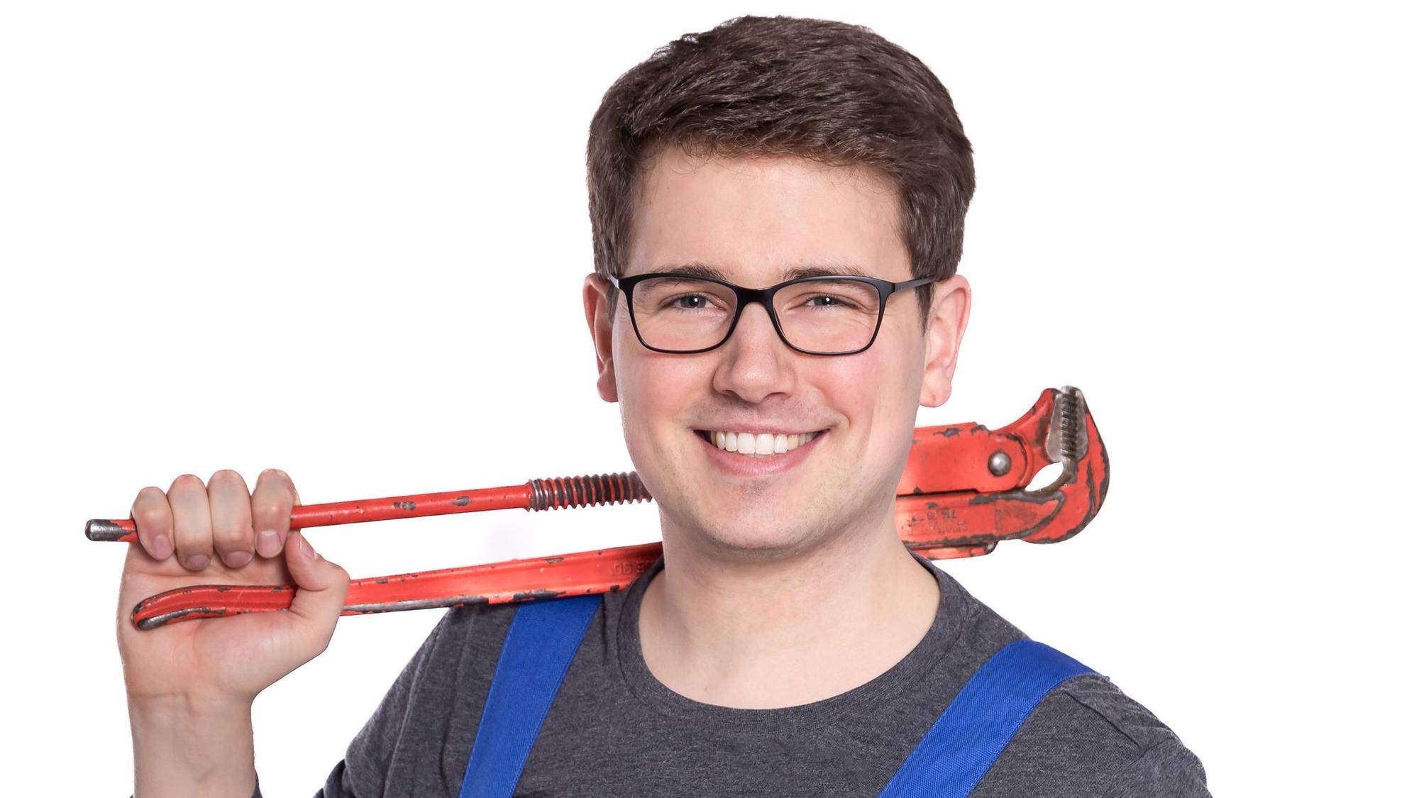 Ein Mann im Blaumann hat eine Zange geschultert und grinst in die Kamera.
