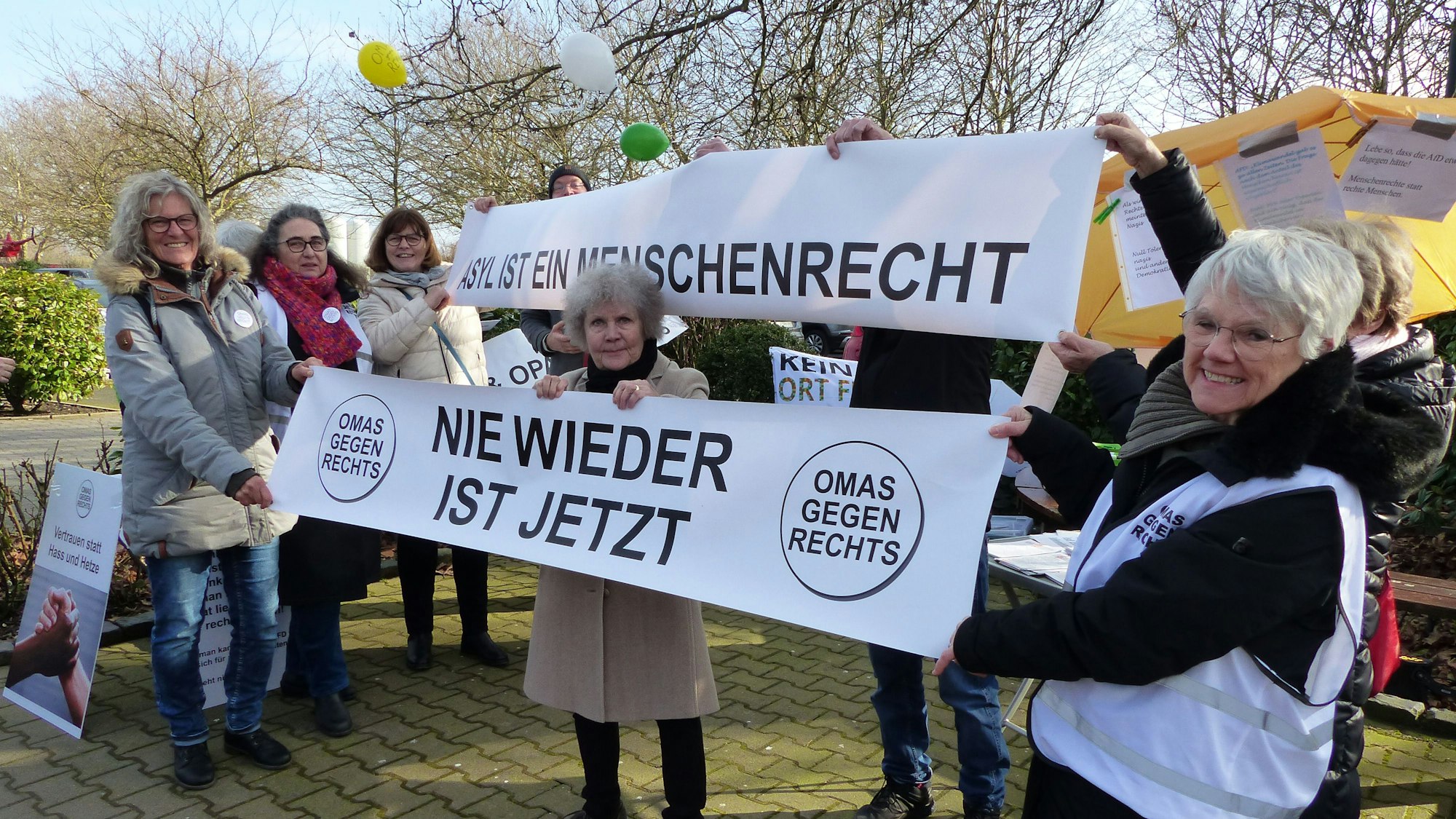 Die Frauen halten Banner mit der Aufschrift „Nie wieder ist jetzt“ und „Asyl ist ein Menschenrecht“ hoch.