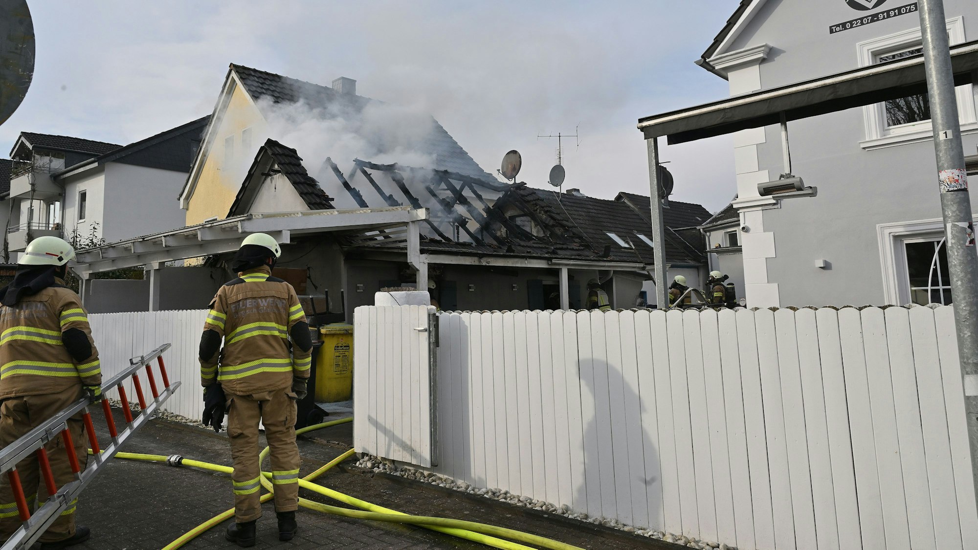 Zwei Feuerwehrleute gehen auf das brennende Haus zu.