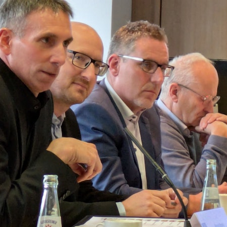 Marcel Wolter, Ingo Pfennings, Norbert Crump und Dr. Hans-Peter Schick sitzen am Tisch und blicken ernst.