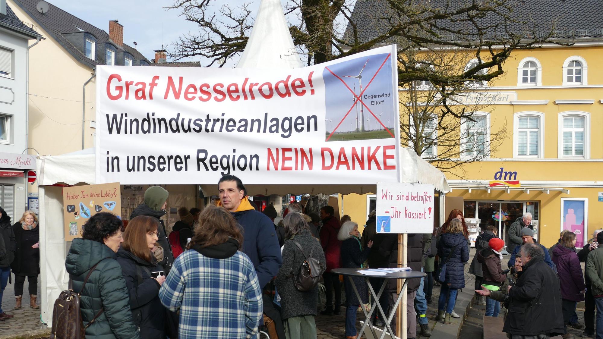 Gegner der rund um Eitorf geplanten Windkraftanlagen stehen mit Transparenten auf dem Eitorfer Marktplatz.