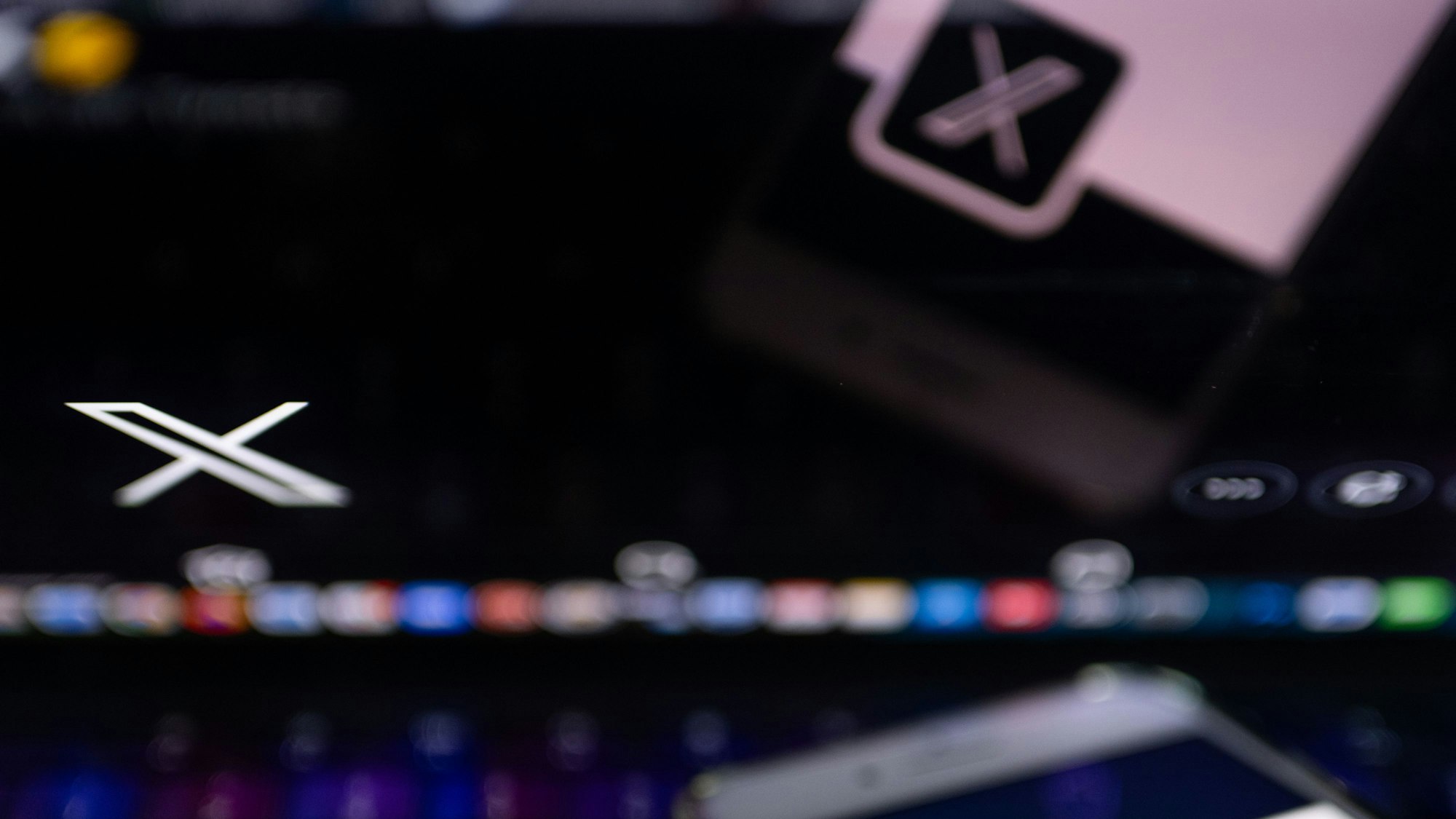 Auf dem offiziellen Profil der Plattform X auf dem Bildschirm eines Smartphones und auf dem Display eines Laptops ist der weiße Buchstabe X auf schwarzem Hintergrund zu sehen,