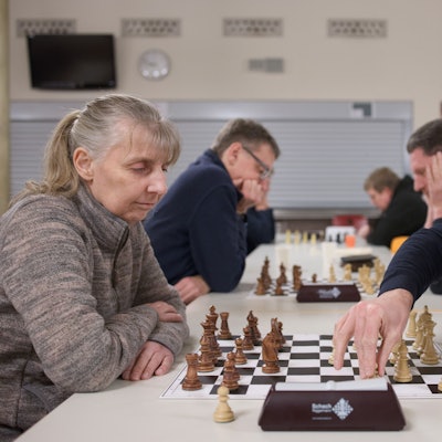 Konzentriert sitzen sich Schachspielerinnen und Schachspieler gegenüber, in der Mitte vor ihnen das Spielbrett mit den Figuren.