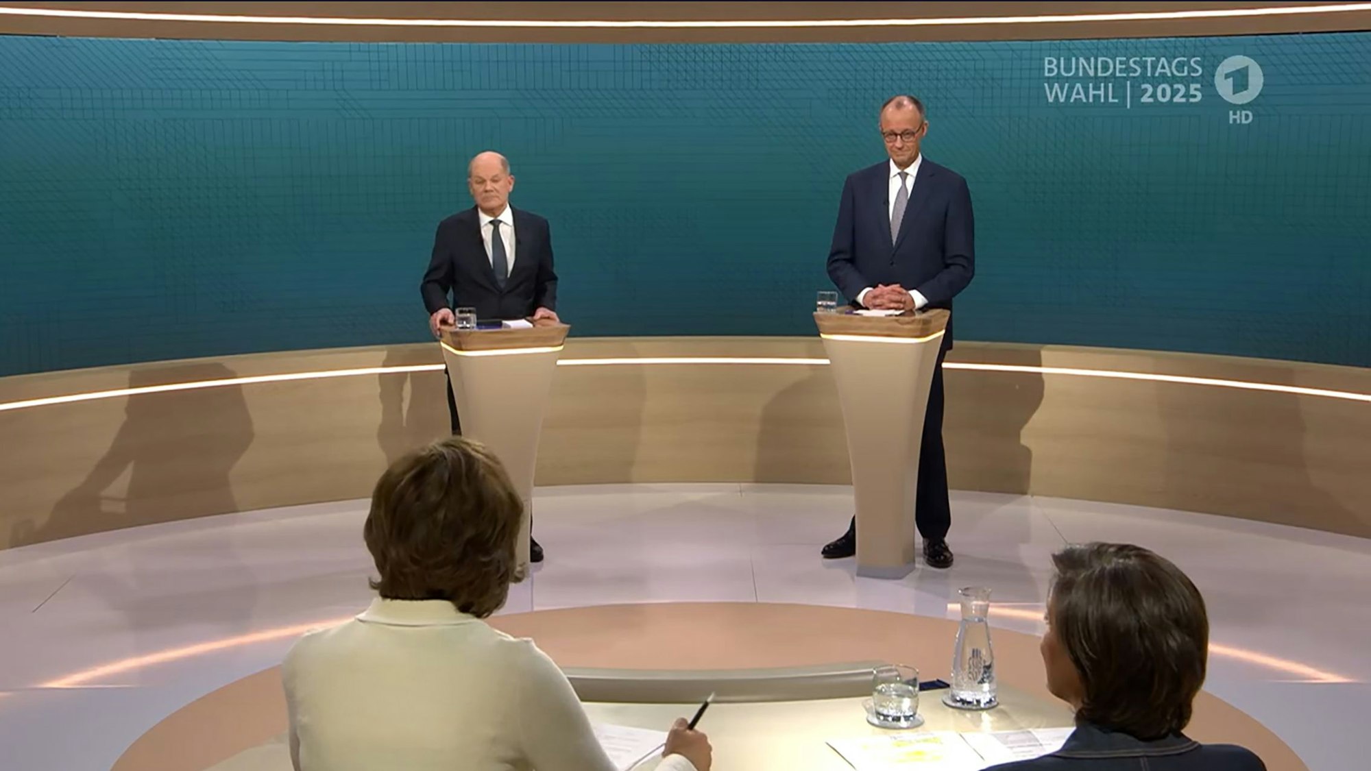 SCREENSHOT - 09.02.2025, Berlin: Bundeskanzler Olaf Scholz (SPD, l), steht neben Friedrich Merz, Unions Kanzlerkandidat und CDU Bundesvorsitzender, während dem TV-Duell von ARD und ZDF (Screenshot). In 90 Minuten stellen sich beide im Studio Berlin-Adlershof zentralen Fragen und debattieren zu den wesentlichen Themen des Bundestagswahlkampfs. Moderiert wird die Sendung von Sandra Maischberger (unten r, ARD) und Maybrit Illner (unten l, ZDF). Foto: ---/ARD/ZDF/dpa - ACHTUNG: Nur zur redaktionellen Verwendung im Zusammenhang mit einer Berichterstattung über die Sendung TV Duell 2025 und nur mit vollständiger Nennung des vorstehenden Credits +++ dpa-Bildfunk +++