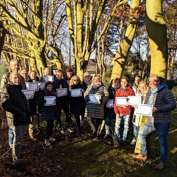 Auf dem Bild ist eine Gruppe von Menschen in einem Wald zu sehen, die Urkunden in den Händen hält.