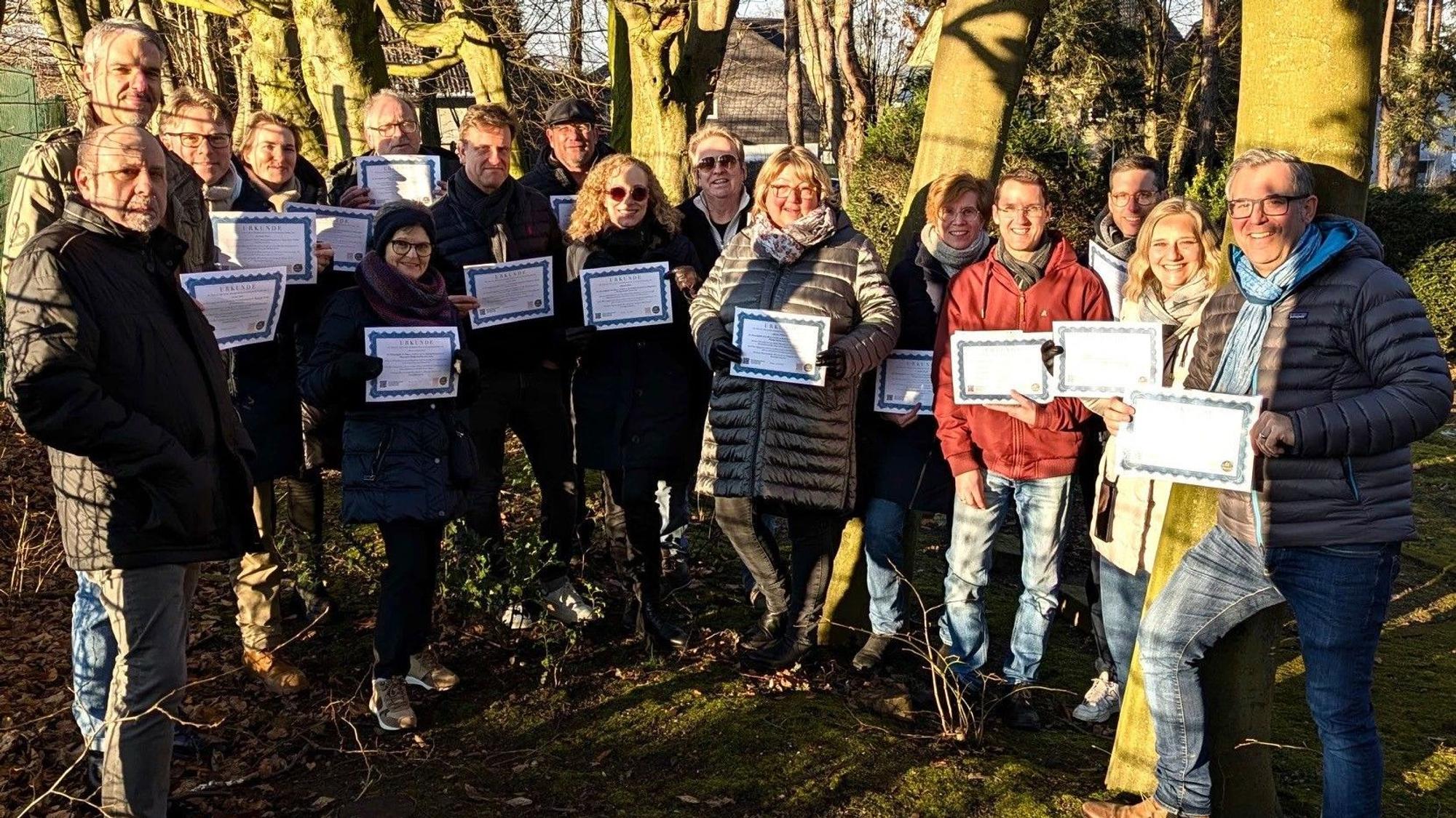 Auf dem Bild ist eine Gruppe von Menschen in einem Wald zu sehen, die Urkunden in den Händen hält.