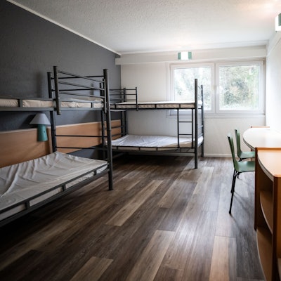 Auf dem Bild ist ein Blick in ein Zimmer mit zwei Stockbetten und einem Tisch mit zwei Stühlen in einer Unterkunft für Geflüchtete in Dortmund zu sehen.