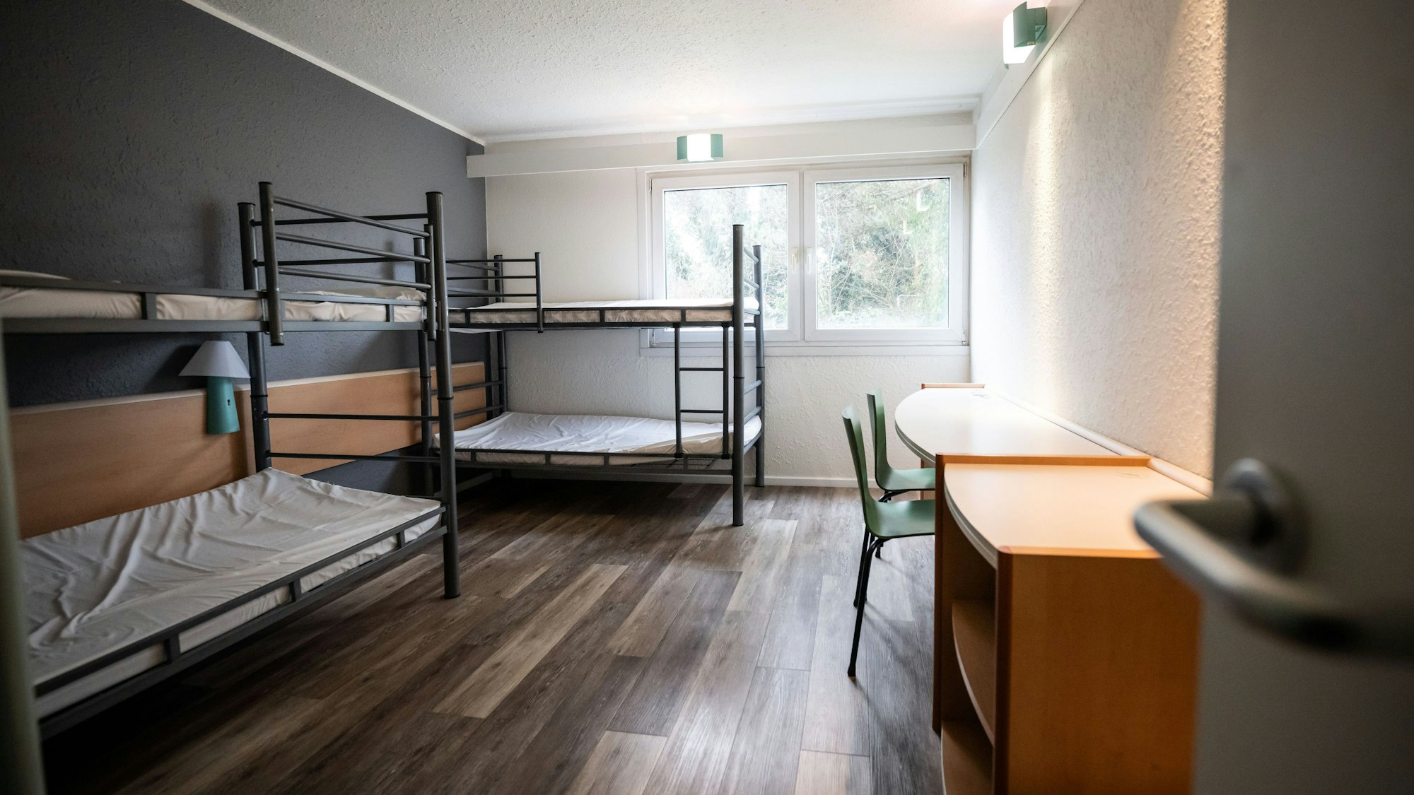 Auf dem Bild ist ein Blick in ein Zimmer mit zwei Stockbetten und einem Tisch mit zwei Stühlen in einer Unterkunft für Geflüchtete in Dortmund zu sehen.