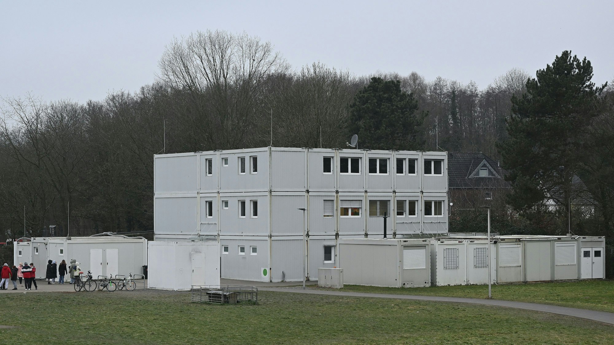 Ein dreistöckiger grauer Containerbau steht auf einer Wiese.