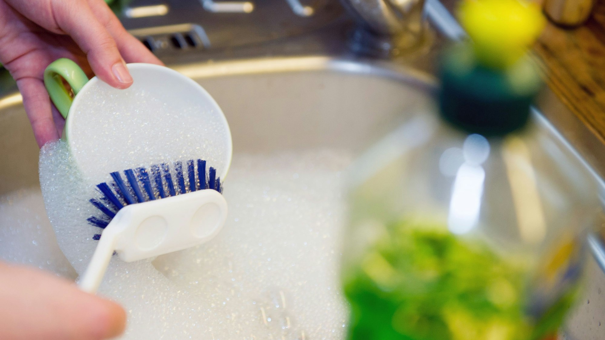 Eine Person wäscht mit Spülmittel und Reinigungsbürste eine Tasse im Spülbecken. (Symbolbild)