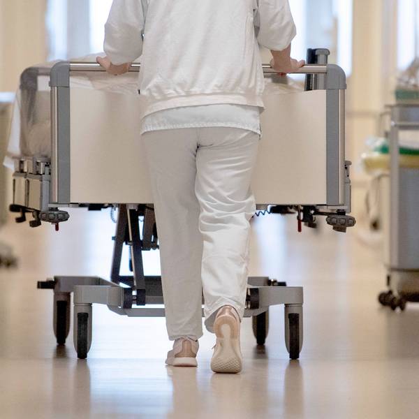 Eine Krankenpflegerin schiebt ein Krankenbett durch einen Krankenhausflur.