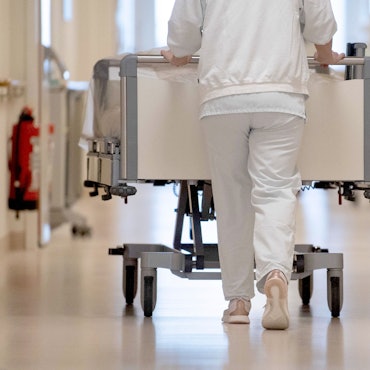 Eine Krankenpflegerin schiebt ein Krankenbett durch einen Krankenhausflur.