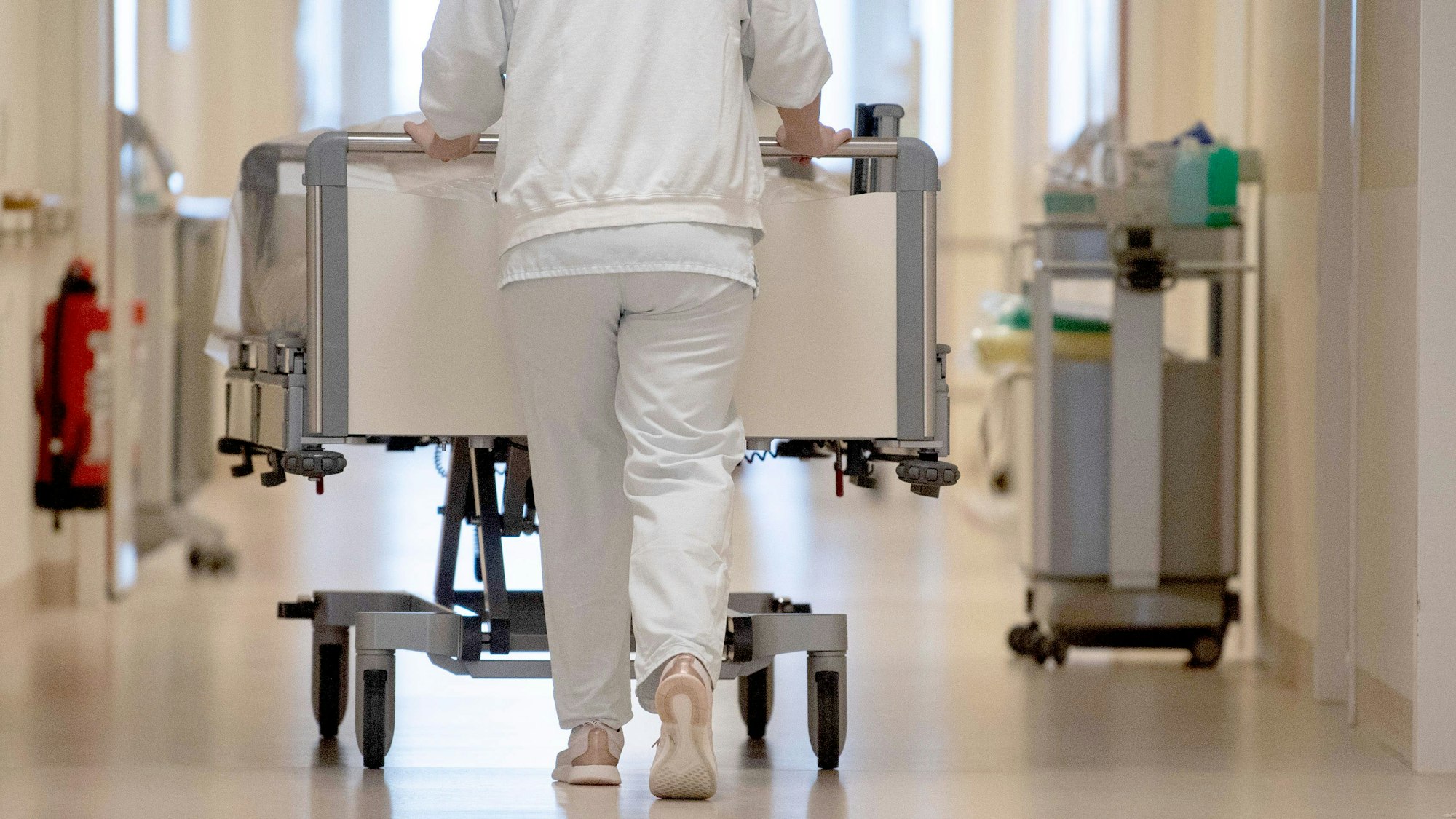 Eine Krankenpflegerin schiebt ein Krankenbett durch einen Krankenhausflur.