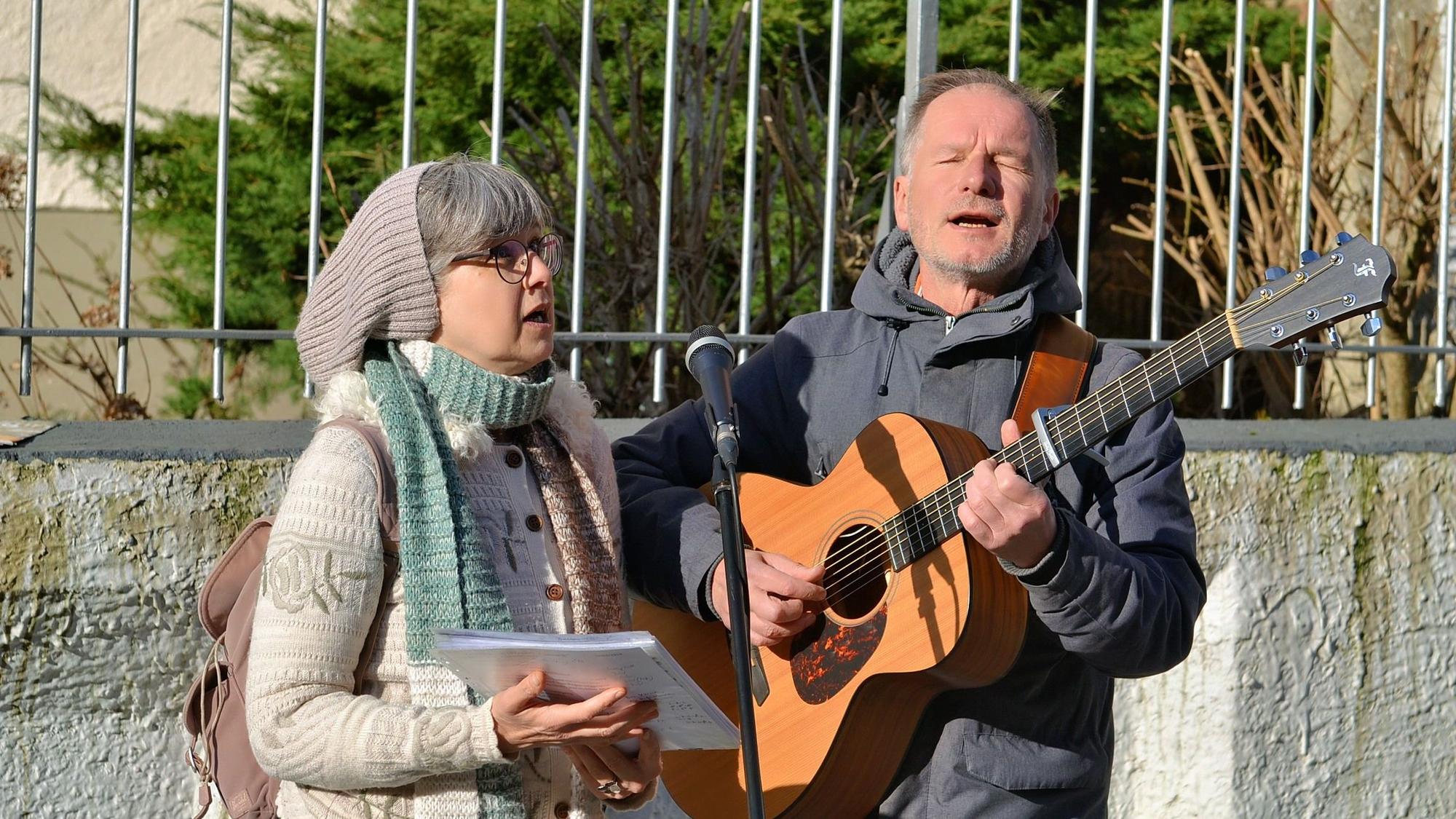 Dagmar Hagmann und Joachim Kubowitz stehen vor einem Geländer, sie singt, er spielt Gitarre und singt ebenfalls.