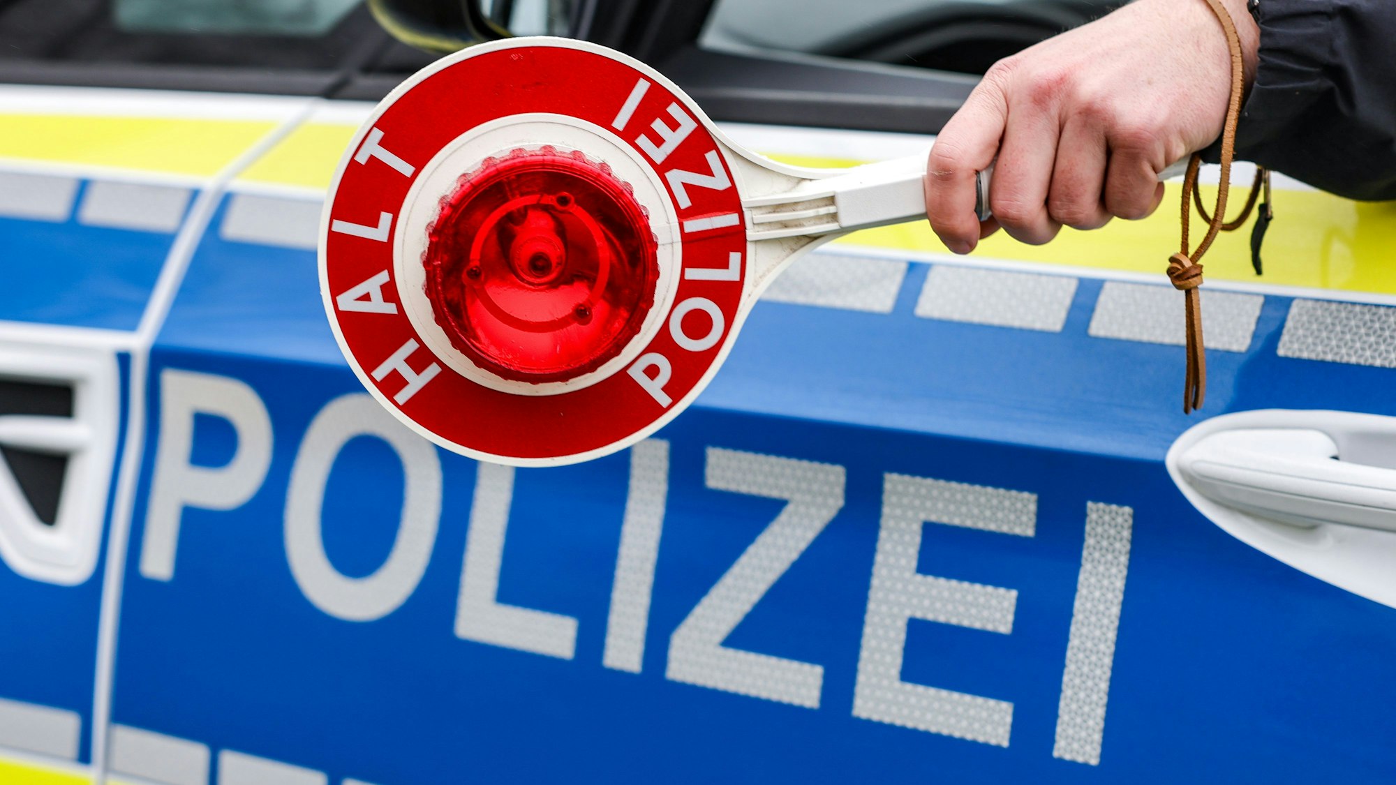 Ein Polizist hält eine Polizeikelle für eine Kontrolle aus dem Streifenwagen.