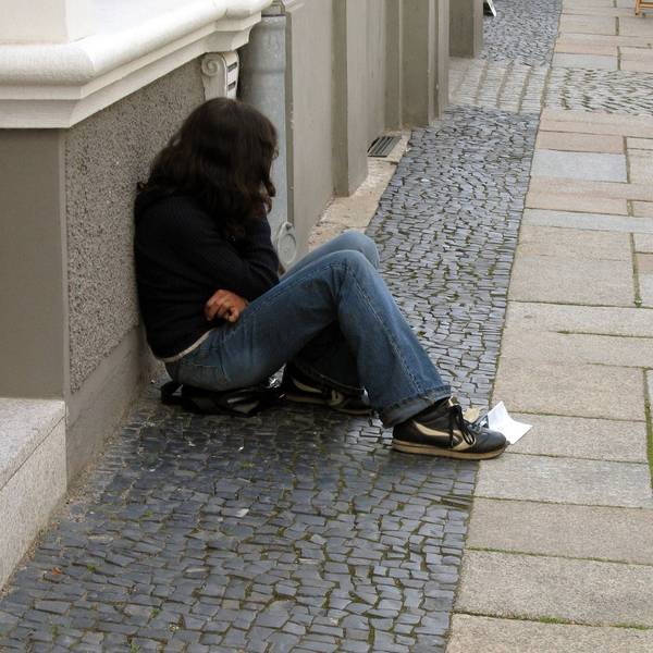 Eine Teenagerin sitzt an eine Hauswand gelehnt auf der Straße.