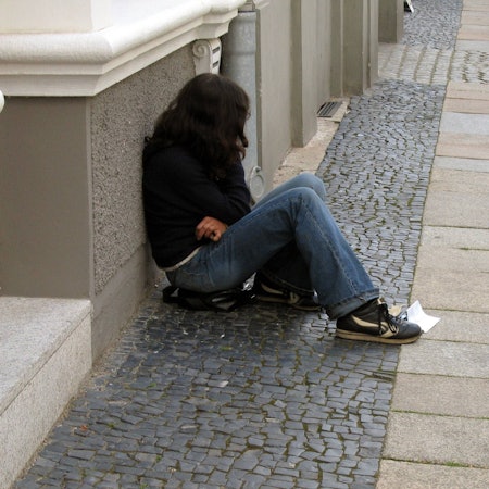 Eine Teenagerin sitzt an eine Hauswand gelehnt auf der Straße.