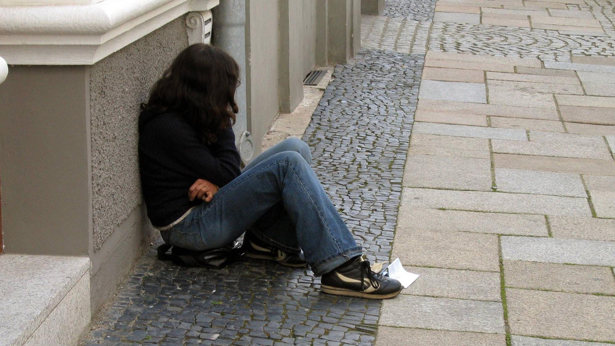 Eine Teenagerin sitzt an eine Hauswand gelehnt auf der Straße.