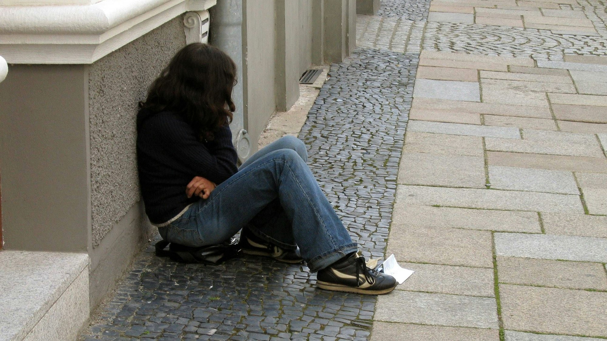 Eine Teenagerin sitzt an eine Hauswand gelehnt auf der Straße.