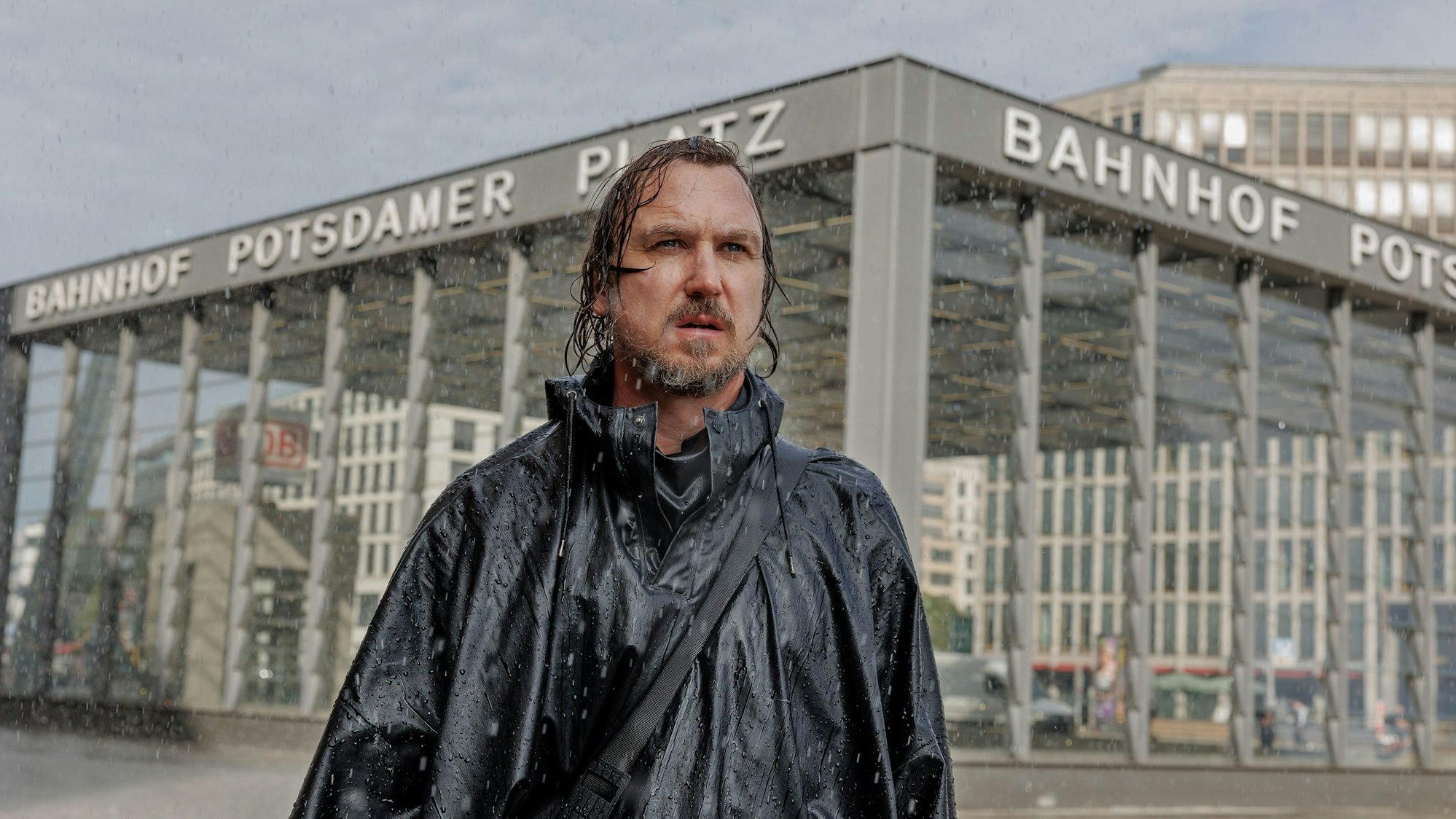 Lars Eidinger steht im Regen vor dem Bahnhof Potsdamer Platz.