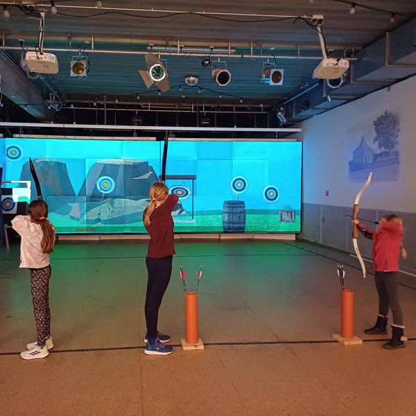 Kinder schießen in einer Halle auf eine Leinwand.