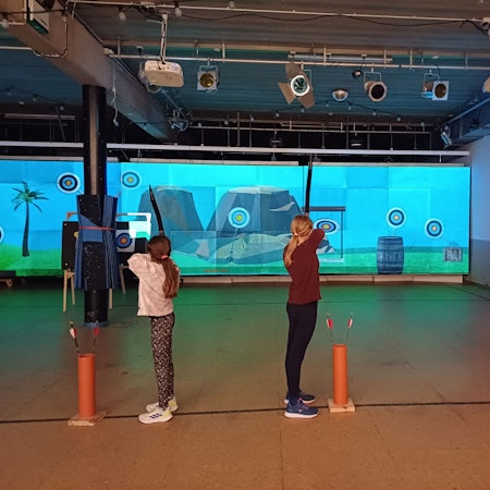 Kinder schießen in einer Halle auf eine Leinwand.