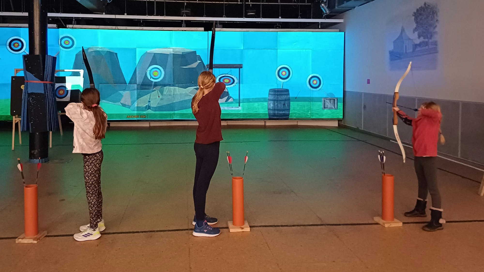 Kinder schießen in einer Halle auf eine Leinwand.