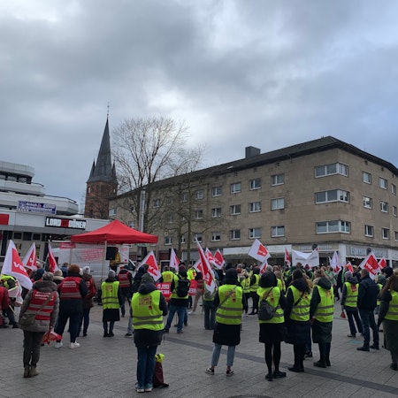 Viele Menschen stehen mit Fahnen und Warnwesten auf einem Platz.