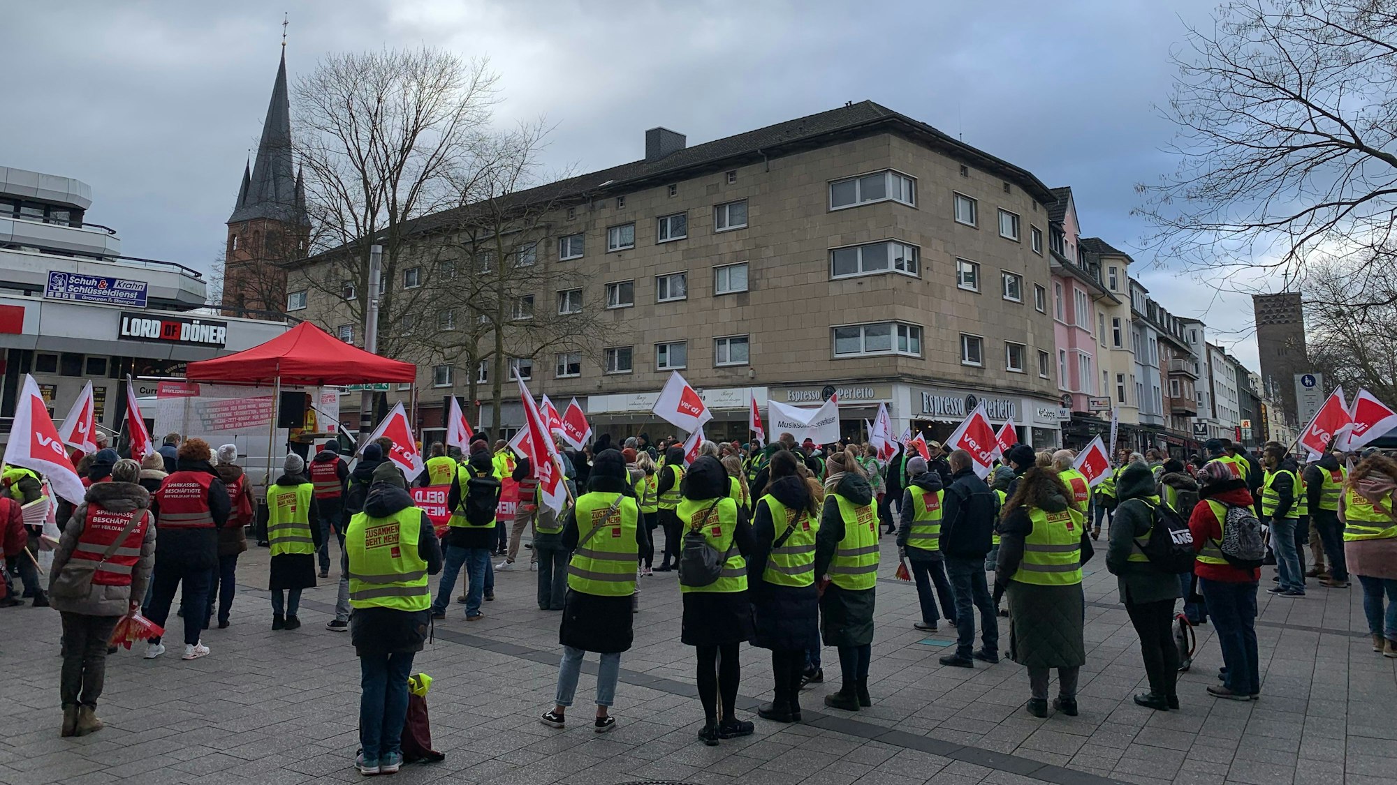 Viele Menschen stehen mit Fahnen und Warnwesten auf einem Platz.