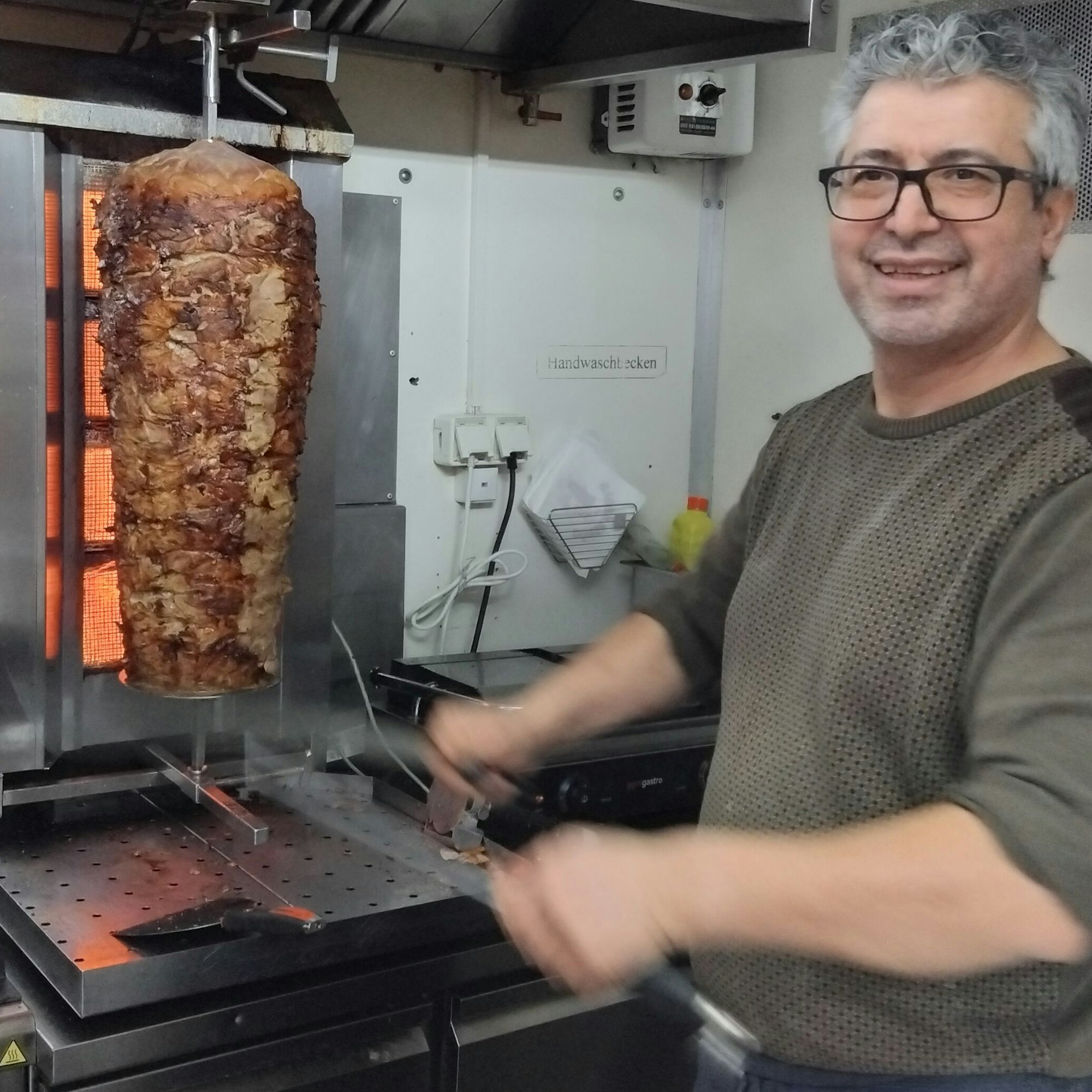 Ein Mann schärft vor einem Döner-Spieß sein Messer.
