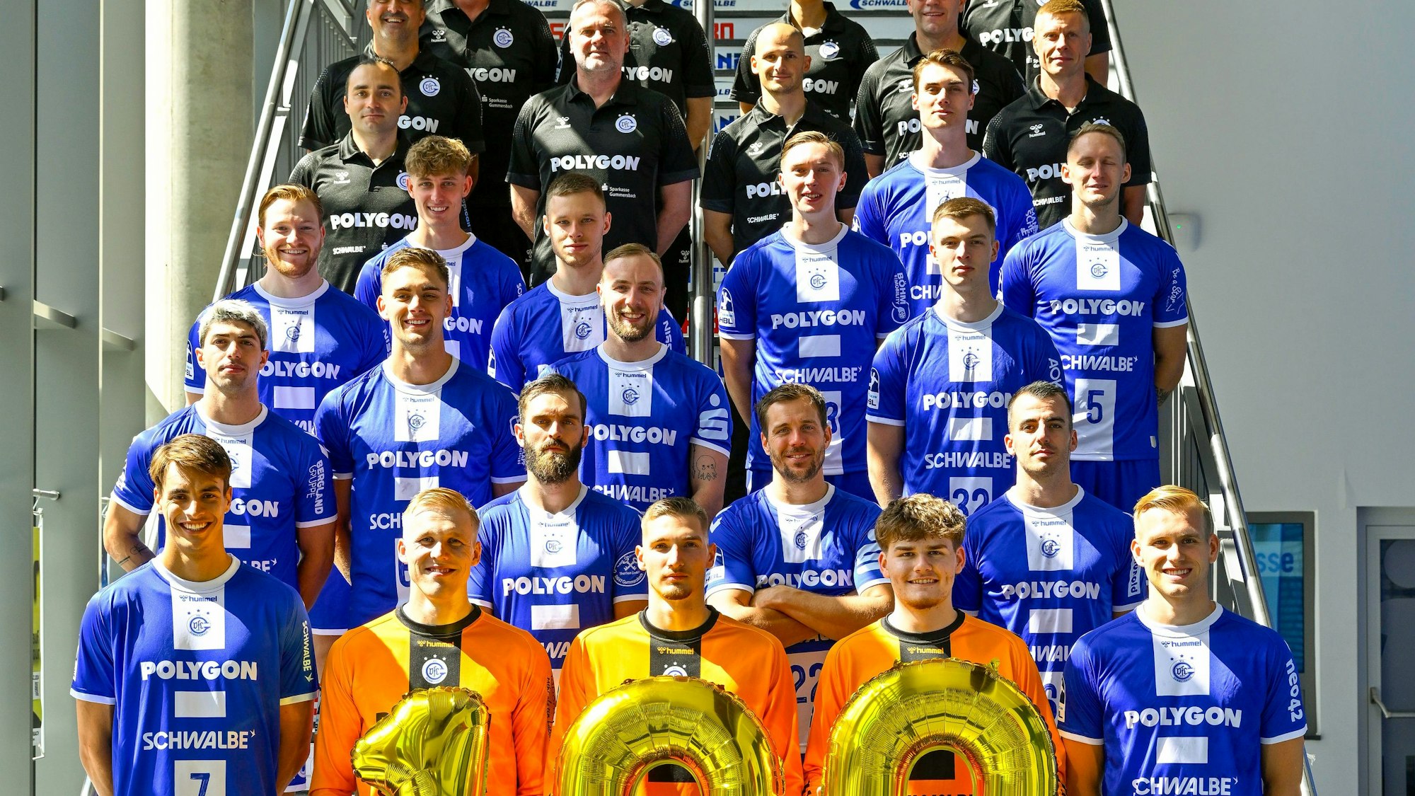Zum Saisonstart haben sich die Handballer des VfL Gummersbach auf der Treppe aufgestellt, die drei Torwarte halten die 100.