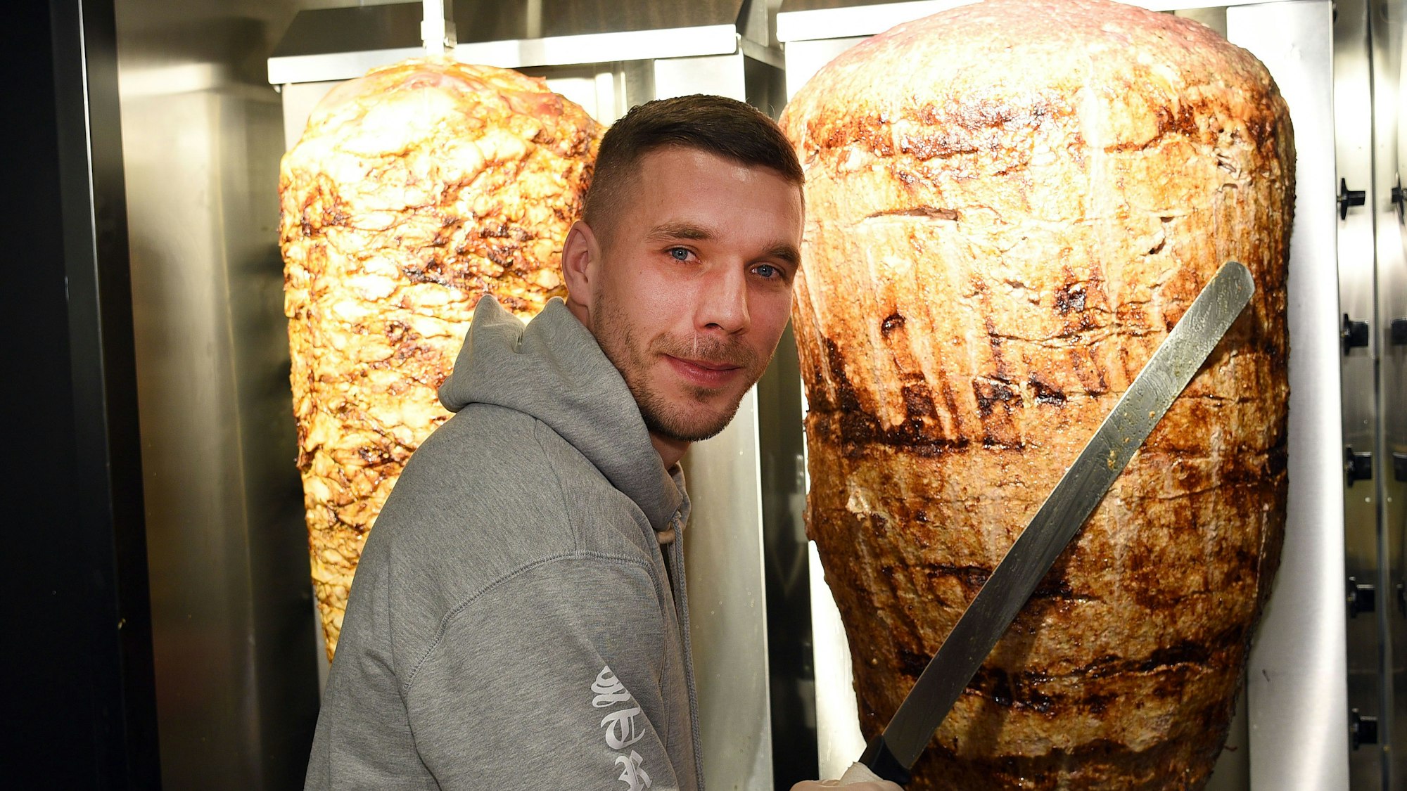 Fußball-Weltmeister Lukas Podolski steht am 6. Januar 2018 in Köln bei der Eröffnung eines Döner-Ladens an einem Dönerspieß.