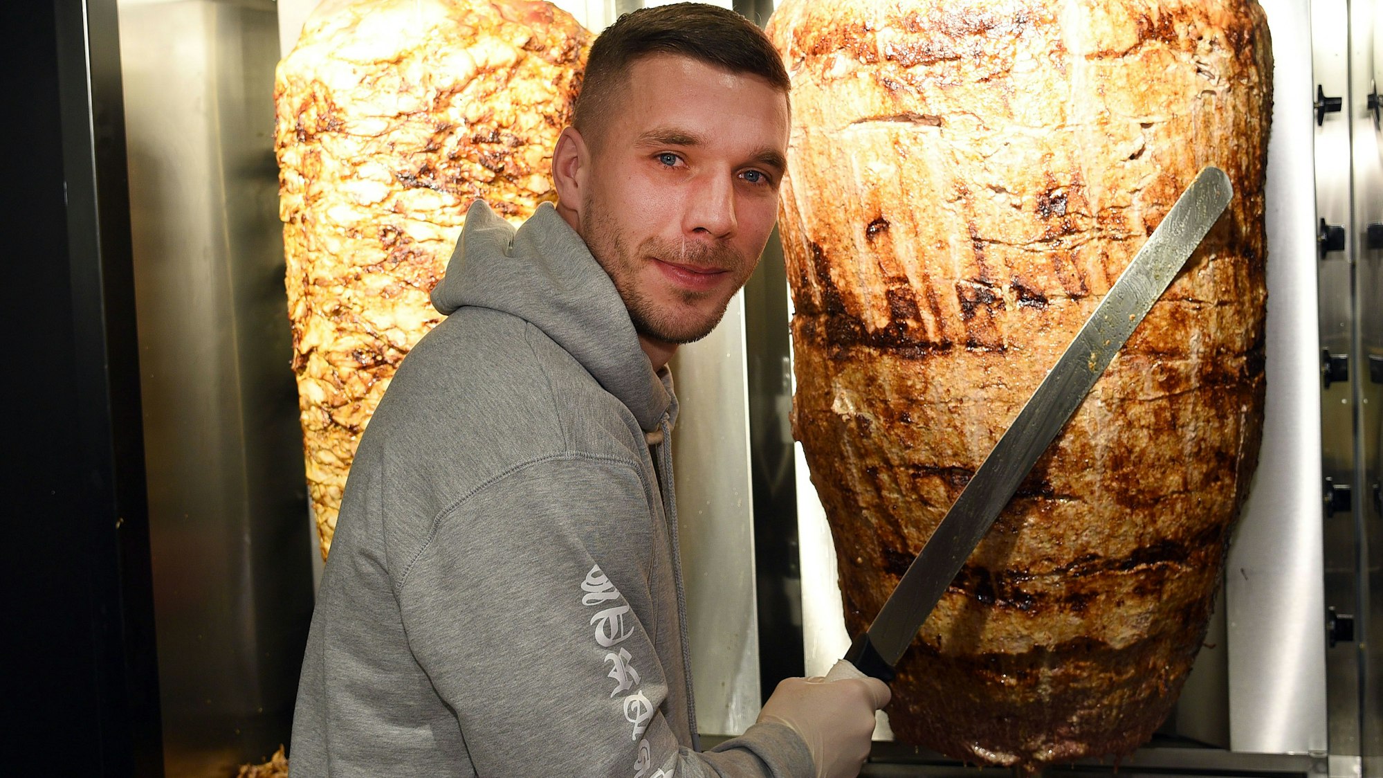 Lukas Podolski steht bei der Eröffnung eines Döner-Ladens an einem Dönerspieß.