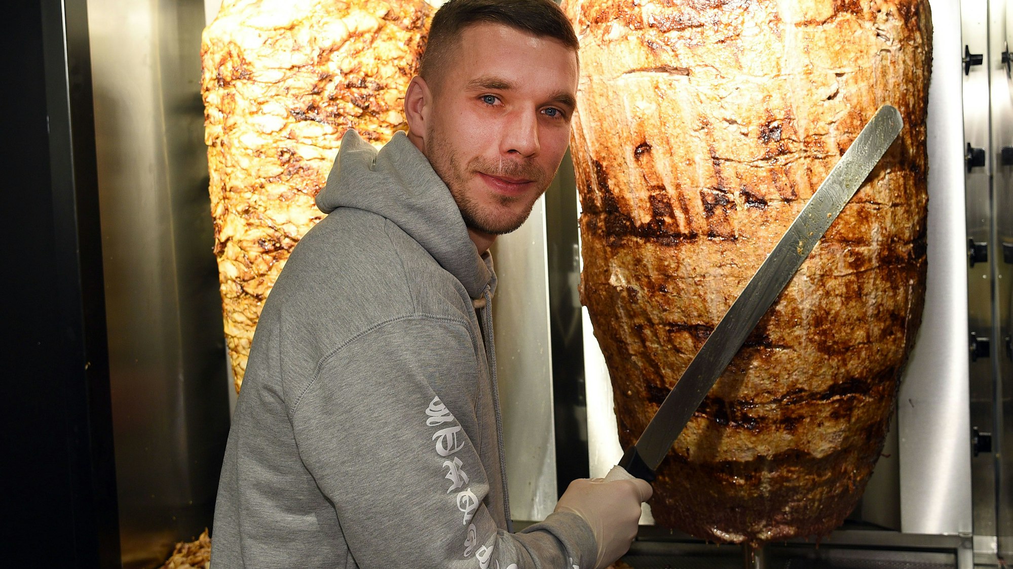 Fußball-Weltmeister Lukas Podolski steht am 06.01.2018 in Köln (Nordrhein-Westfalen) bei der Eröffnung eines Döner-Ladens an einem Dönerspieß.