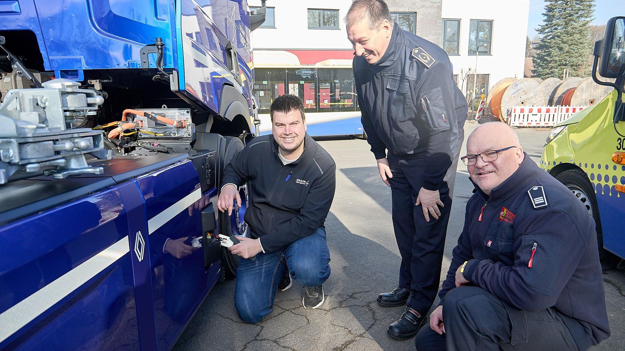 Drei Männer stehen an einem blauen Elektrofahrzeug und betrachten den Knopf zum Abschalten.