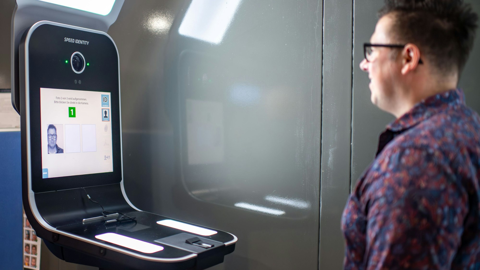 Das Bild zeigt einen Mann, der vor einem Gerät steht, das ein Foto aufnimmt.