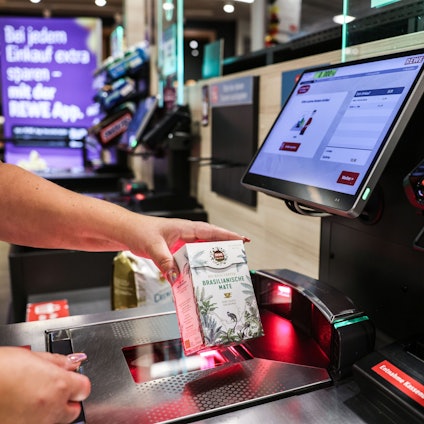 Eine Frau scannt  ein Produkt an einer Selbstbedienungskasse.