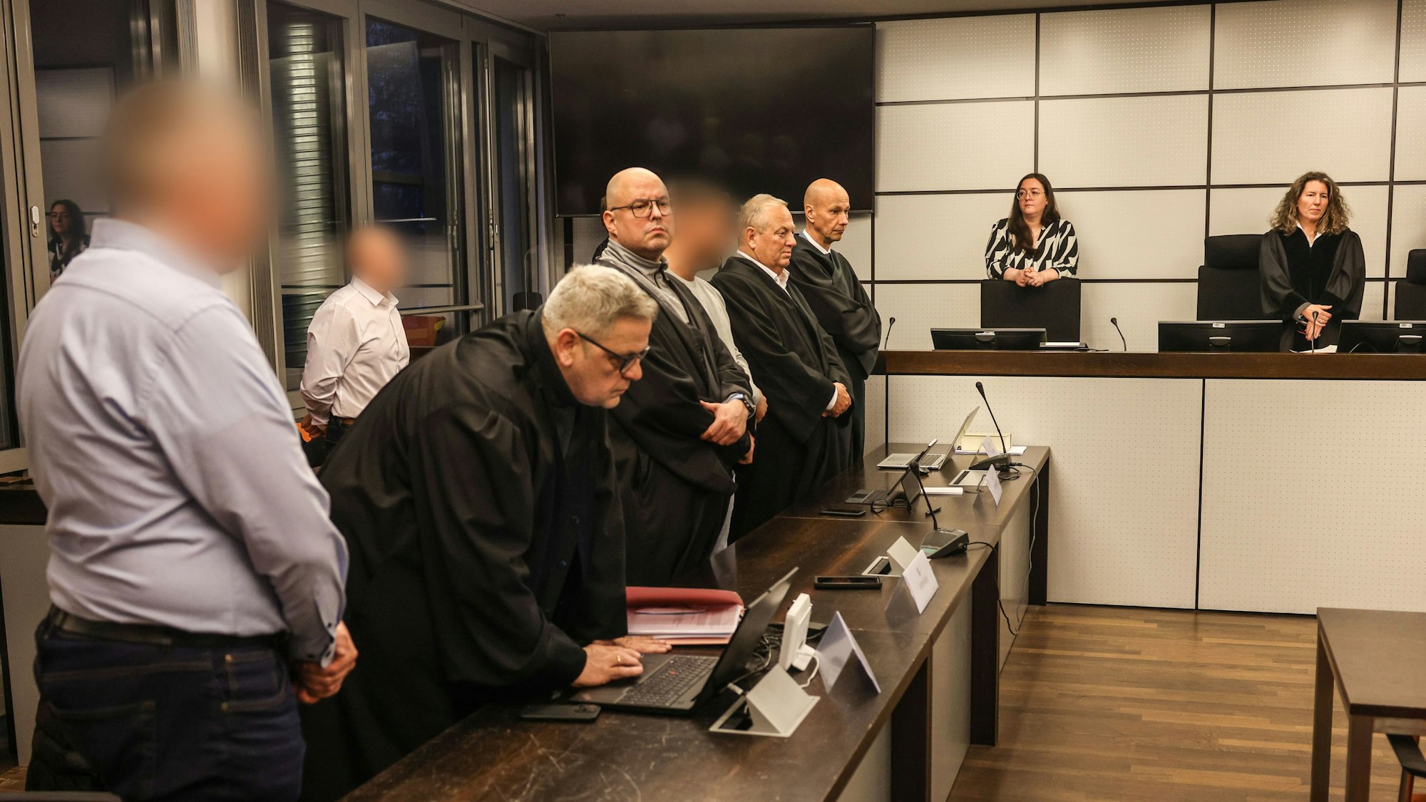 Die drei Angeklagten (l, hinten l sowie 4.v.l) stehen vor der Urteilsverkündung im Gerichtssaal des Amtsgerichts zwischen Anwälten.