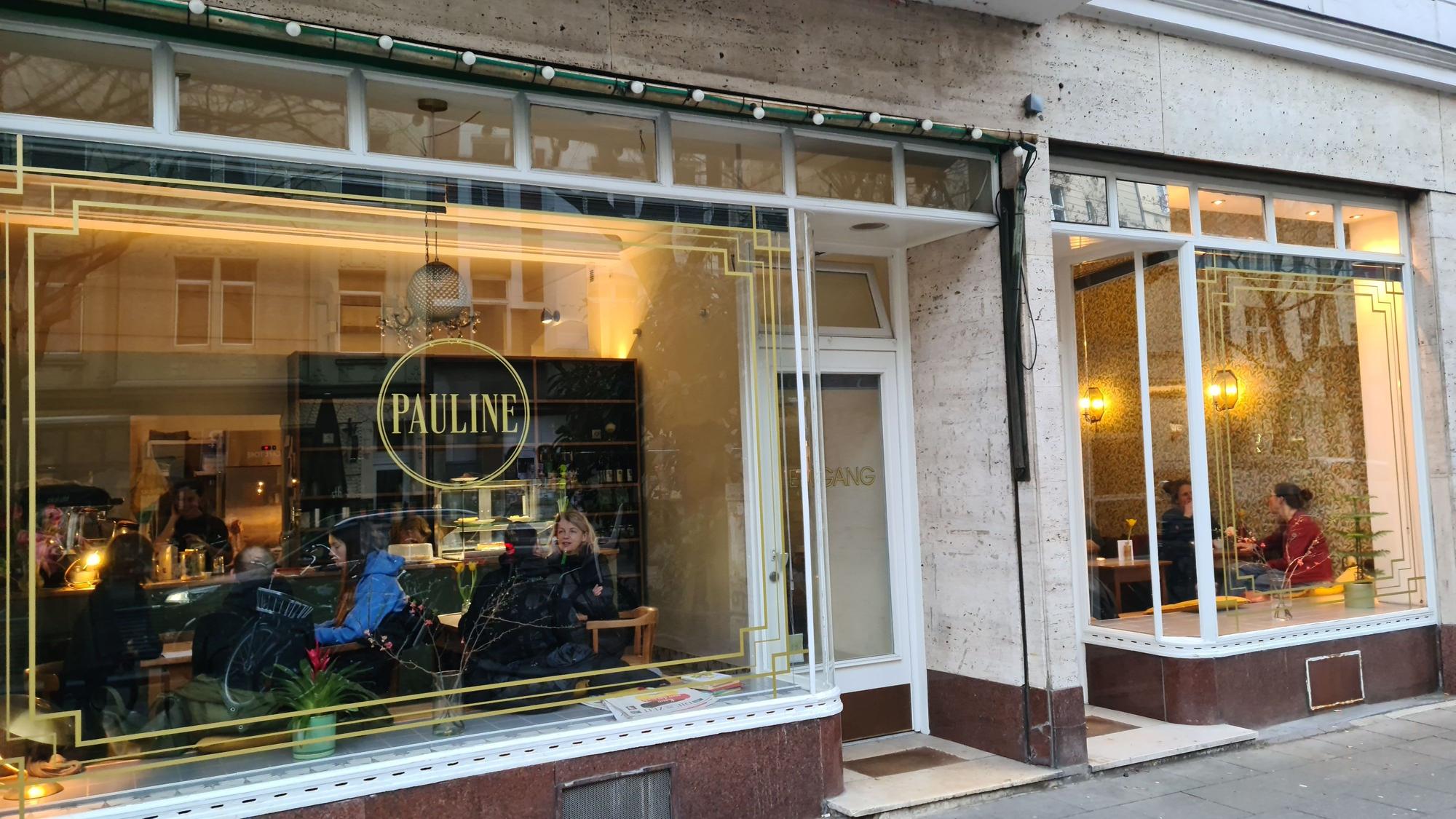 Blick auf eine Fensterfront eines Cafés; in Goldbuchstaben und oval umrandet steht der Schriftzug Pauline auf einem Fenster.