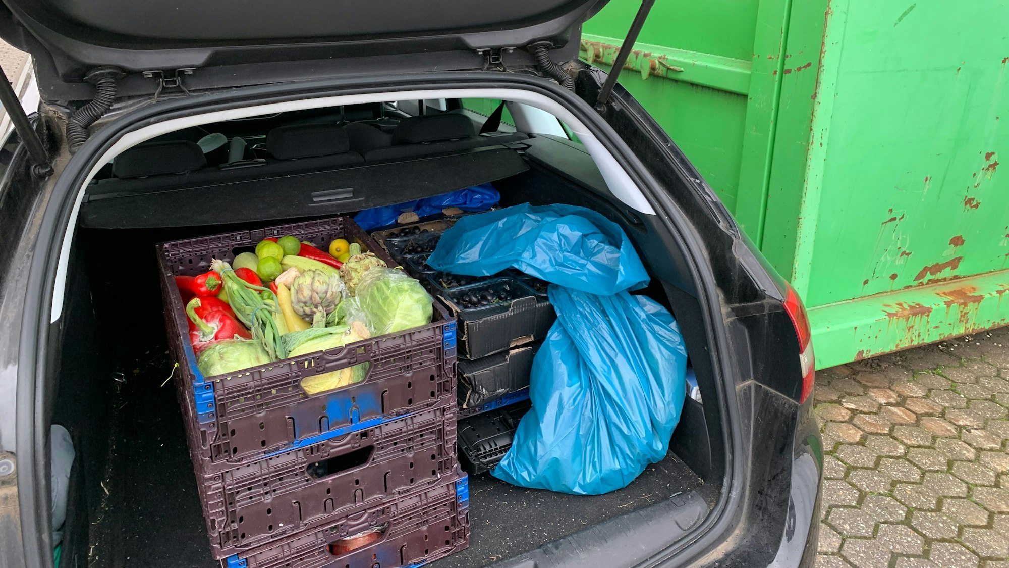 Mehrere Kisten mit Obst und Gemüse stehen im Kofferraum eines Autos.