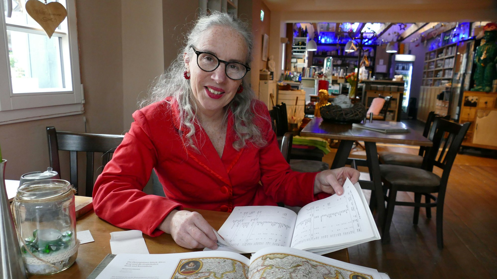 Eine Frau in roter Jacke sitzt in einer alten Gaststube vor Büchern.