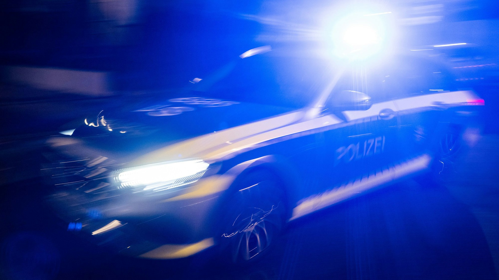 Ein Polizeifahrzeug fährt mit Blaulicht an einem Gebäude vorbei.