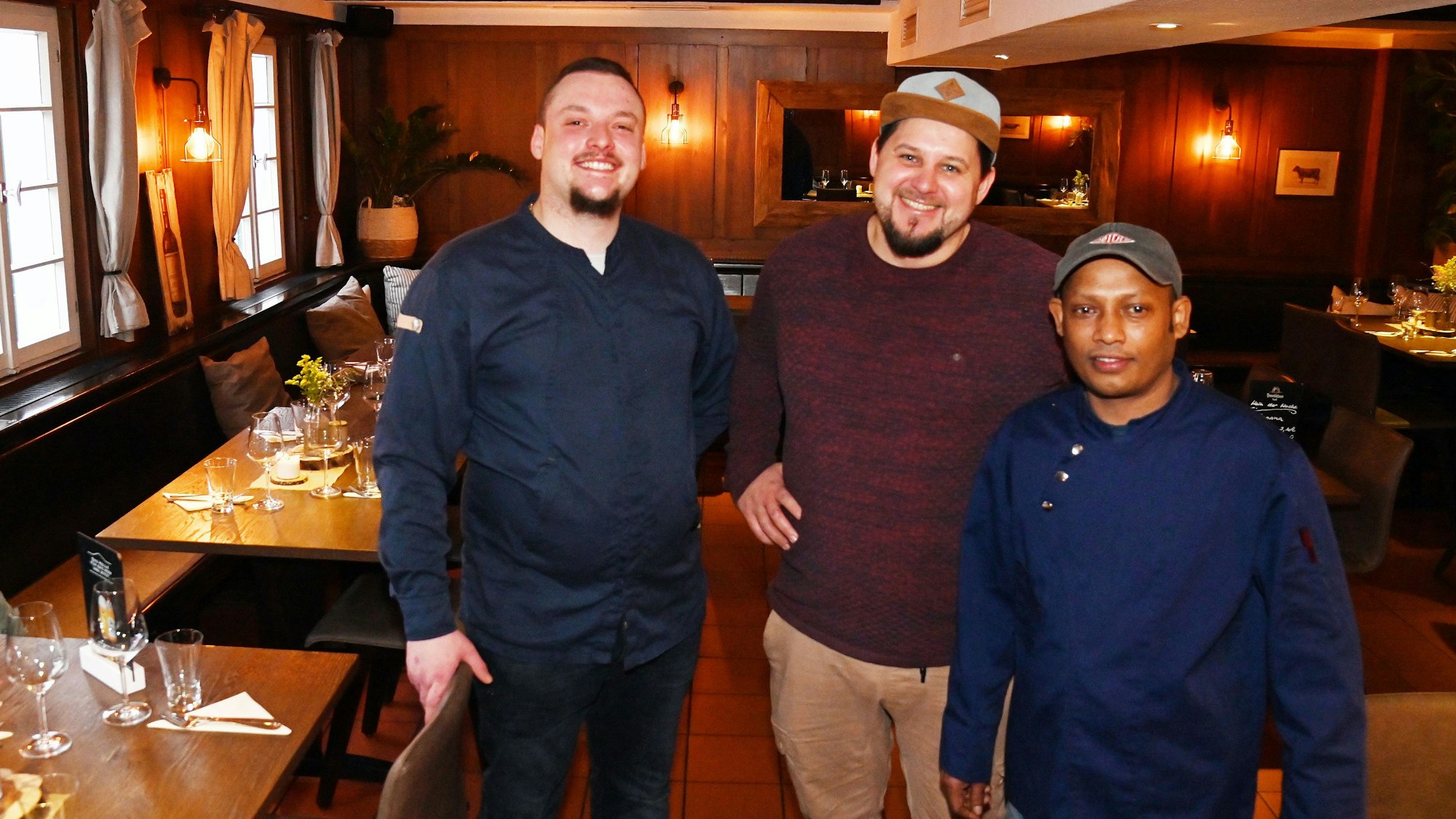 Die drei Männer sind in der rustikalen Gaststube zu sehen.