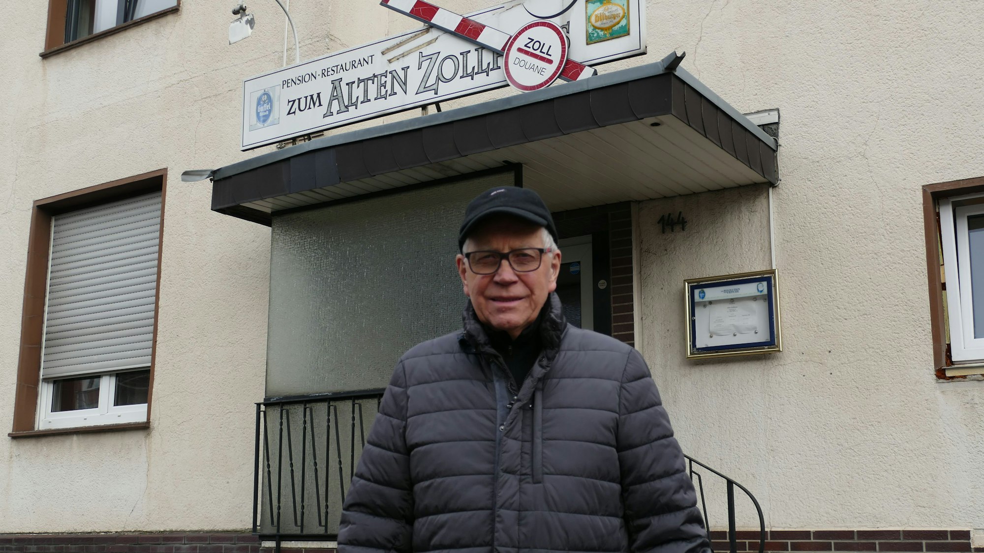 Ein Mann steht vor einer Gaststätte, die den Namen „Zum Alten Zoll“ trägt.