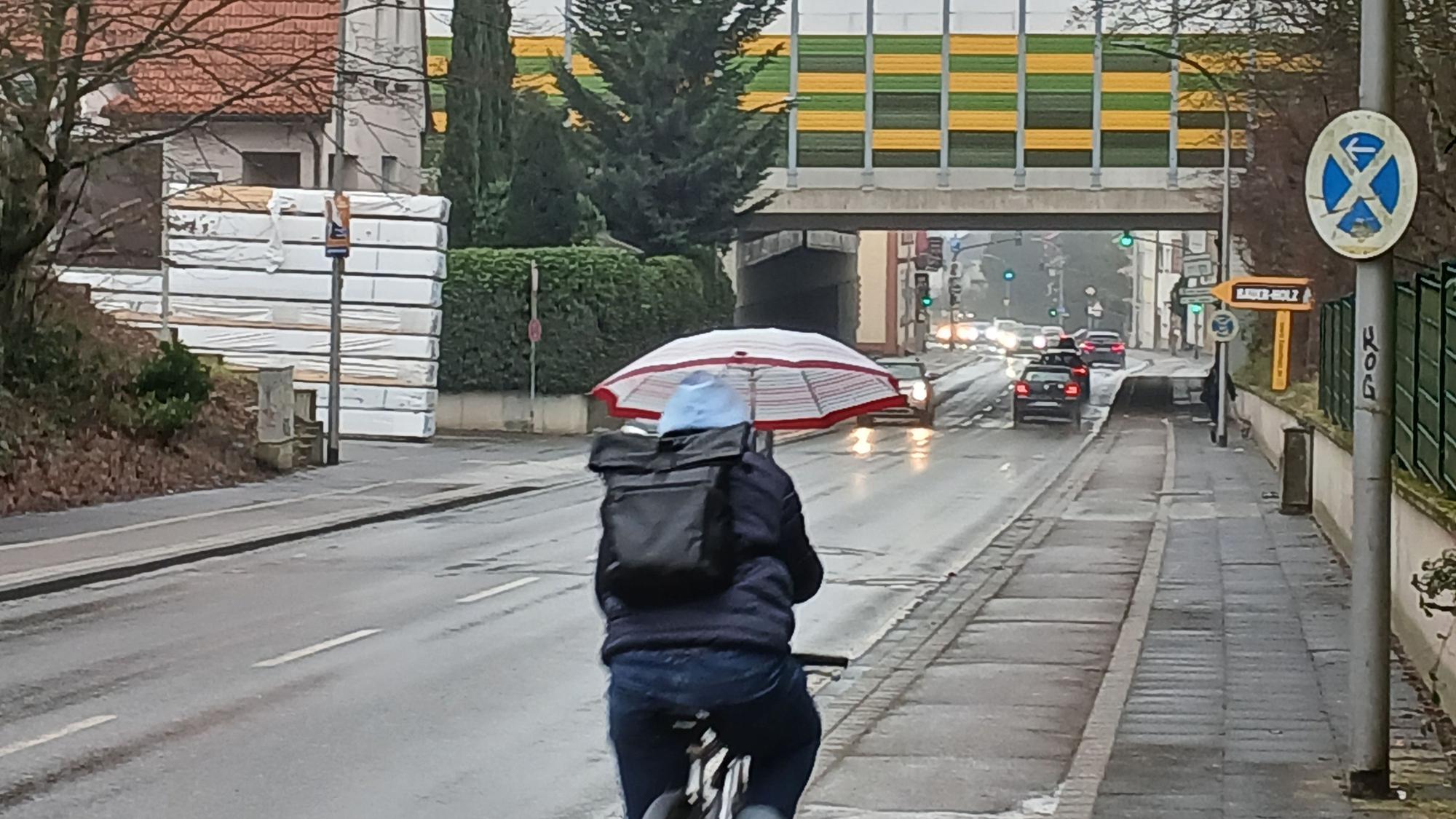 Ein Radfahrer hält einen Regenschirm und fährt eine Straße entlang.