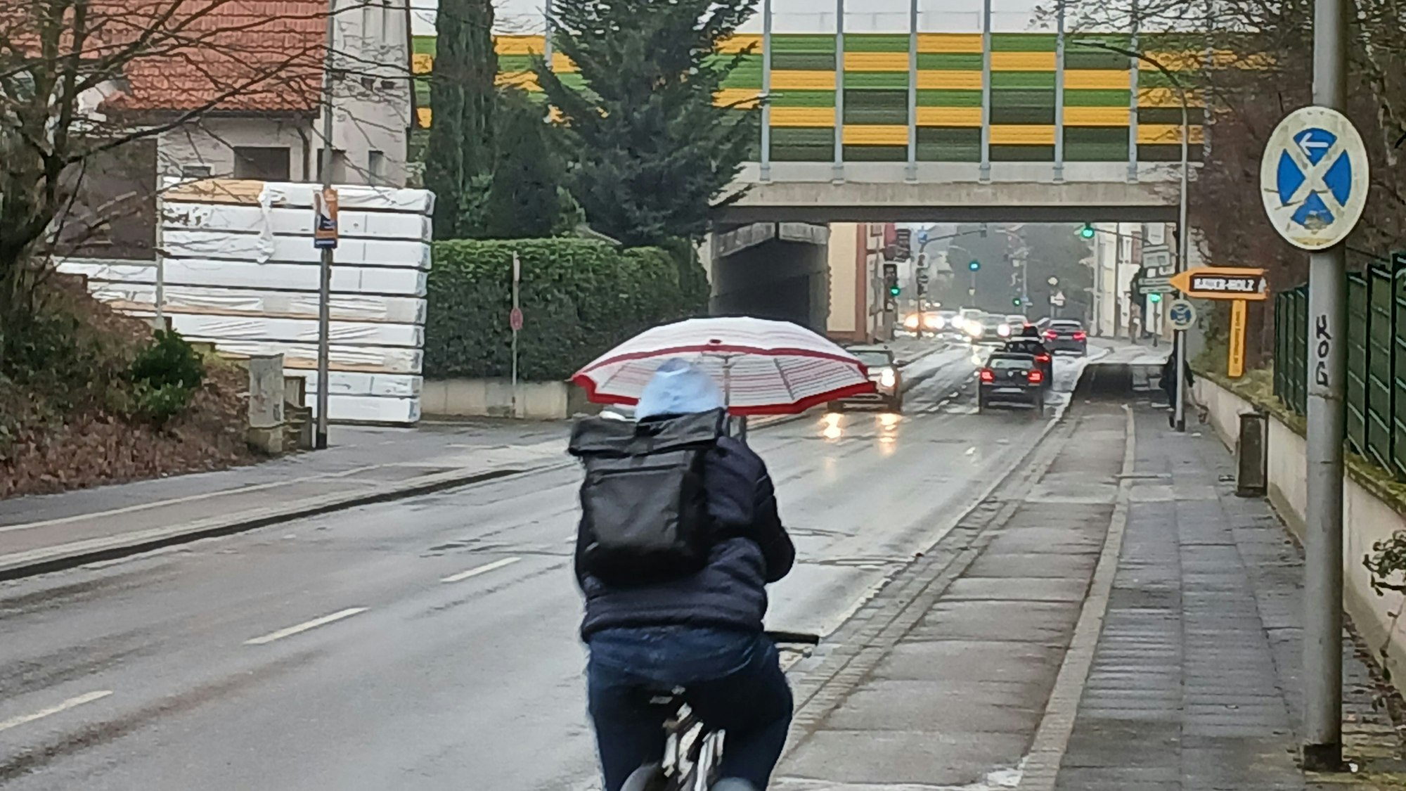 Ein Radfahrer hält einen Regenschirm und fährt eine Straße entlang.