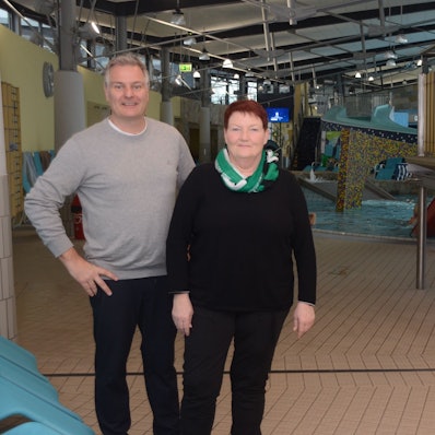 Ein Mann und eine Frau stehen in einem Hallenbad am Rand eines Kinderbeckens.