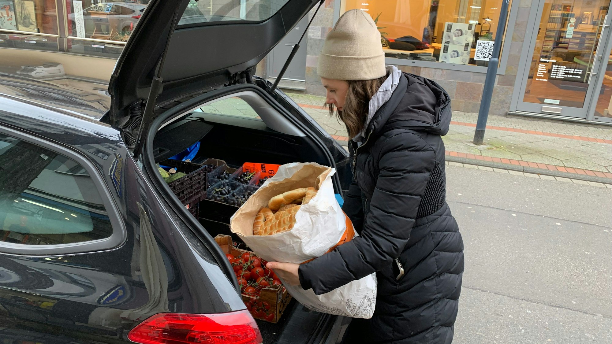 Eine Frau legt einen großen Papiersack mit Gebäck in den Kofferraum eines Autos.